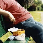 Mid-Section of an Overweight Man Sitting on a Park Bench With Take-Away Food